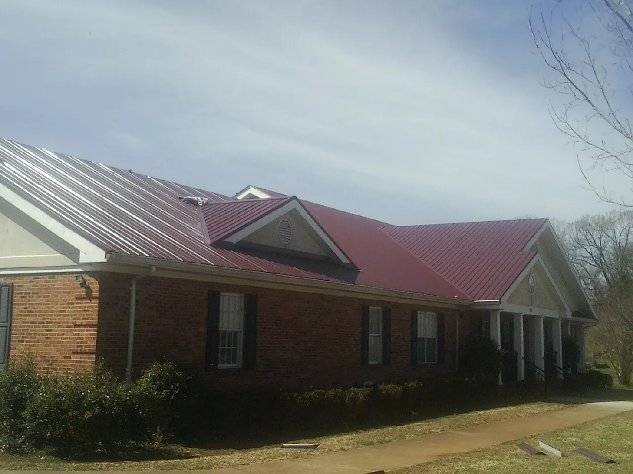 Red metal roof with gabled entries on a long brick building, from a Hail Damage Roof Repair job in Tekoa
