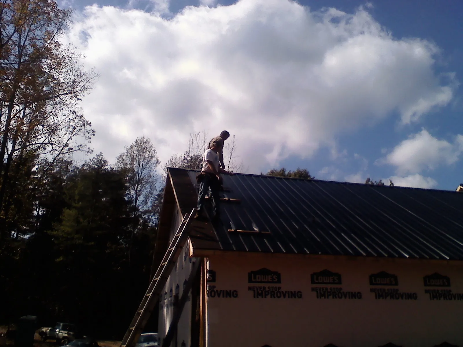 Roofer fastening dark metal panels high against a cloudy sky, from a Roof Inspection job in Tekoa